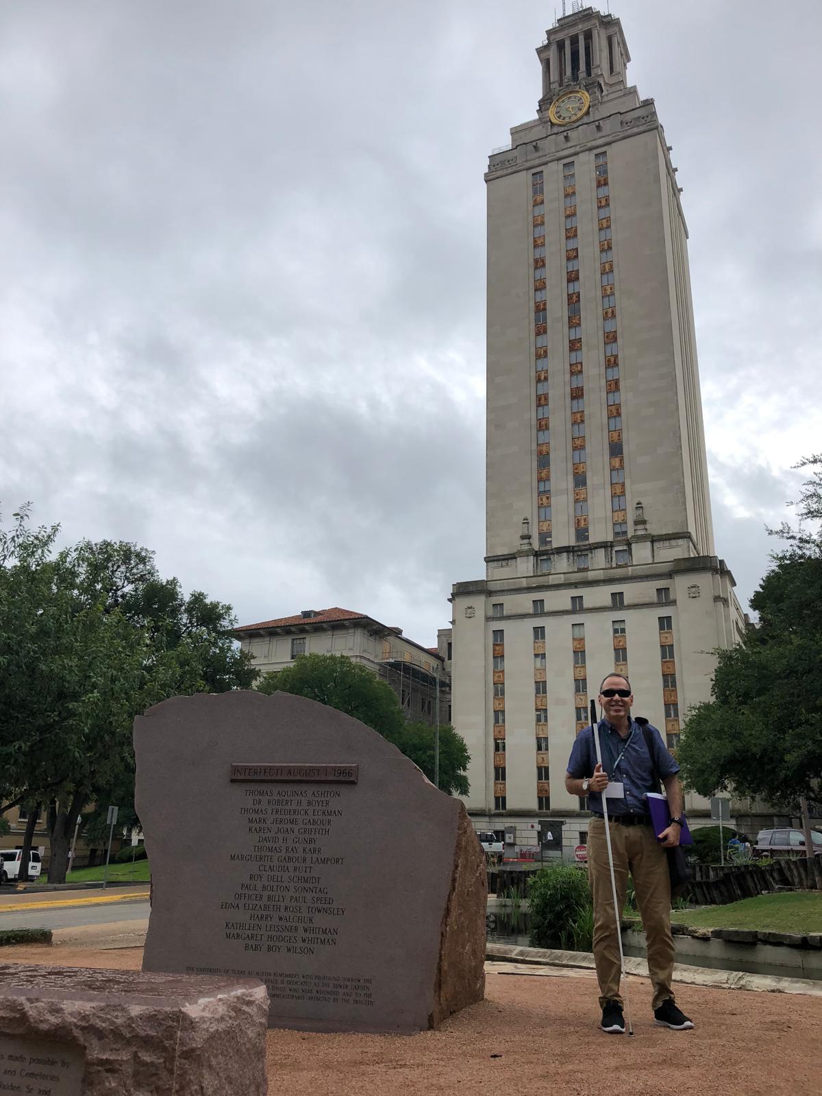 Foto de Manolo posando al lado de una torre alta con un reloj en la parte superior, que es el icónico edificio de la Universidad de Texas en Austin.